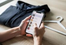 Ruke drže mobilni telefon iznad sklopljene crne dukserice i plastične vešalice