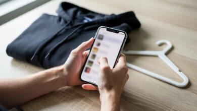 Ruke drže mobilni telefon iznad sklopljene crne dukserice i plastične vešalice
